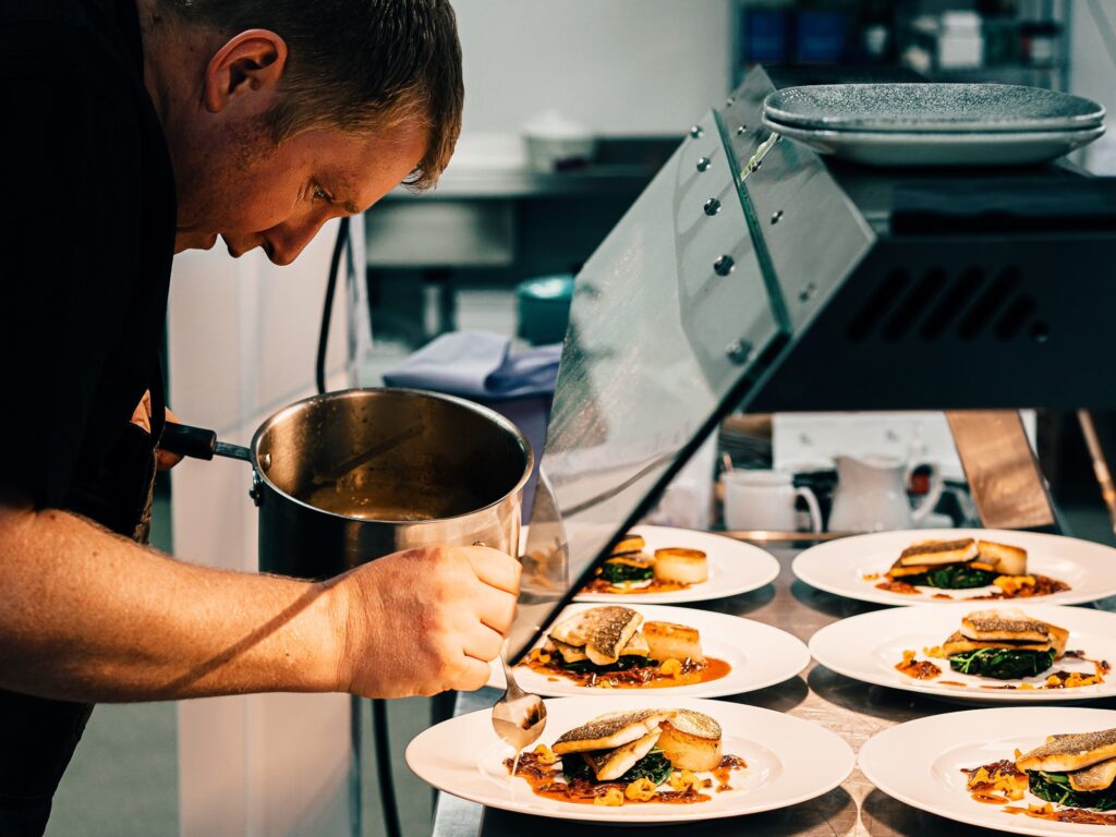 An image of a man working in a commercial kitchen, surveying plates of prepared food.