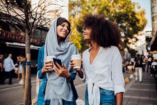Two women walking downtown, drinking coffee