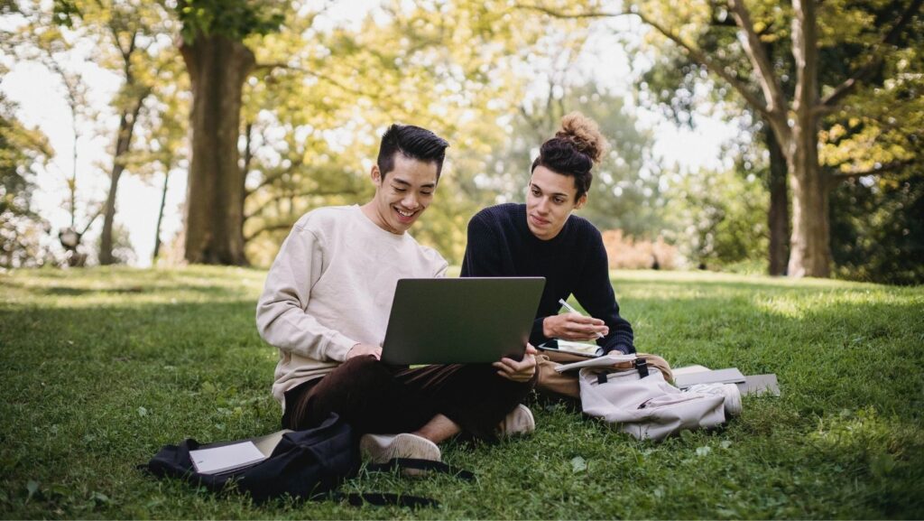 international students sitting outside looking at a laptop