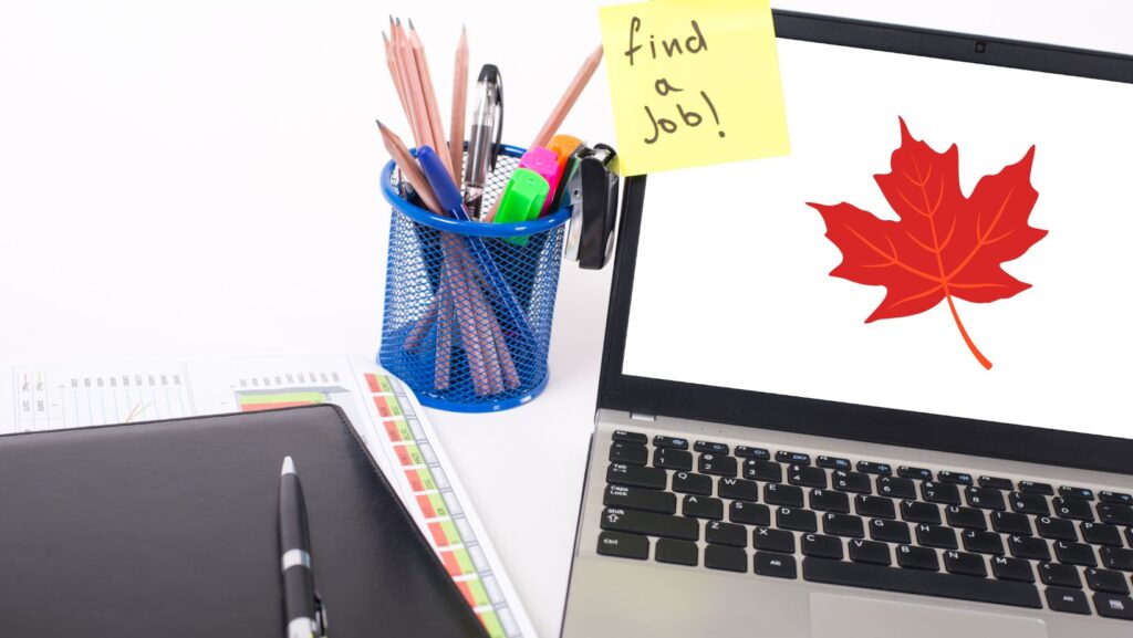 A laptop with a maple leaf on the screen and a sticky note that says "find a job!"